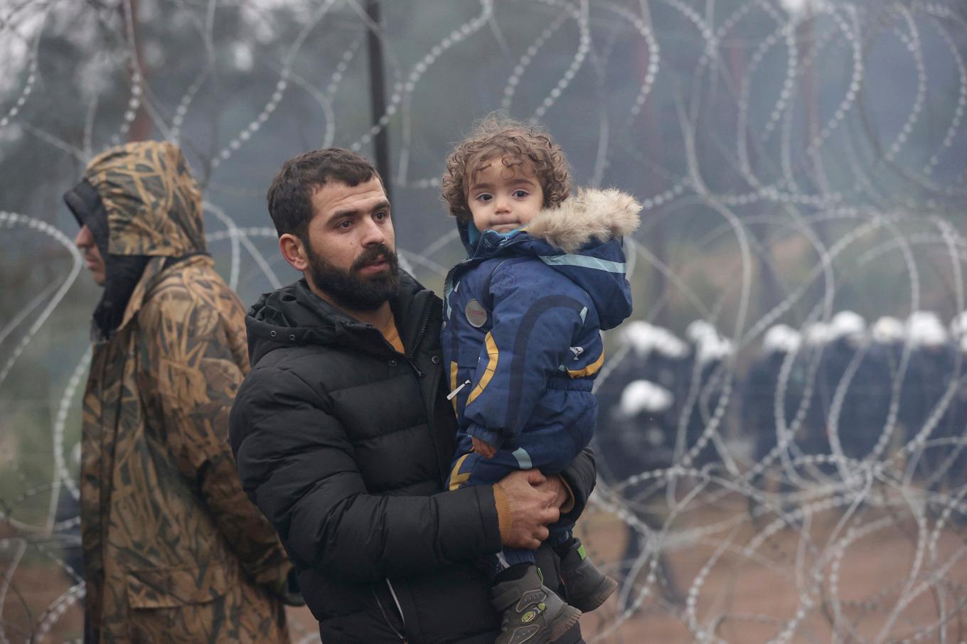 En pappa och hans barn vid taggtrådsstängslet som skiljer Belarus från EU-landet Polen. De senaste åren har Polen sett en ökning av migranter vid gränsen. Bild tagen i november 2021. Foto: Oksana Manchuk/AP/TT