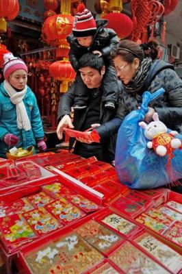 De röda kuverten är viktiga inslag i det kinesiska nyårsfirandet. Den kinesiska familjen studerar butikens urval. (Foto: Philippe Lopez / AFP)