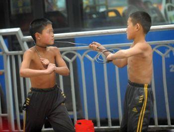 Två pojkar som uppträder på gatan i Chongqing, den 9 februari. En av pojkarna lindar ståltråd runt den andres hals. (Foto: Epoch Times/arkivbild)
