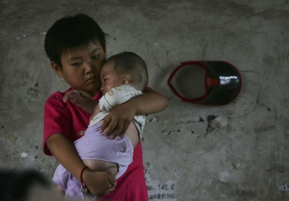 Tioåriga Wang Huaixue håller ett mindre barn på Wang Jiayu-barnhemmet i Anhuiprovinsen i Kina, 9 juli 2006. ”Efterlämnade barn”, barn till migrantarbetare som lämnas i hembyn, är vanligt förekommande i Kina, och leder till många problem. (Foto: China Photos/Getty Images)