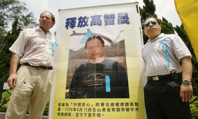 Edward McMillan-Scott, vice talman i Europaparlamentet, vid en bild av den i Kina fängslade människorättsadvokaten Gao Zhisheng, taget under en kampanj för Gaos frigivande i Hongkong  år 2006, efter att McMillan genomfört ett människorättsuppdrag i Kina. Till höger människorättsadvokaten Albert Ho. (Foto: Mike Clarke/AFP/Getty Images)