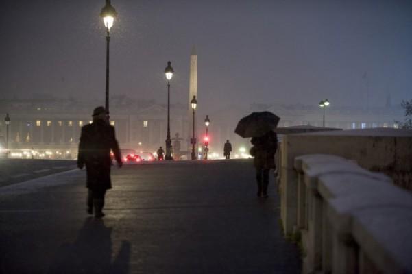 Människor går på den snötäckta bron Pont de la Concorde i Paris. Många har bevittnat hur offentlig gatubelysning på ett mystiskt sätt har mörknat när någon passerar förbi under. Alltmedan de här personerna med åren har börjat dela sina erfarenheter har fenomenet blivit känt som Street Light Inteference (SLI). (Fred Dufour/AFP/Getty Images)