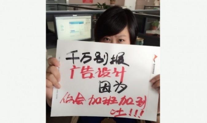 En ung kines håller upp en handmålad skylt med texten "Välj inte reklamdesign – all övertid kommer att få dig att kräkas". Den här sortens varningar har blivit virala på internet i Kina på sistone. (Skärmdump från Weibo)