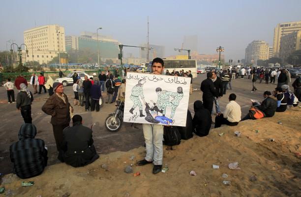 En egyptisk demonstrant på Tahrirtorget i Kairo den 19 december, håller i en banderoll med texten "(fältmarskalk  Mohammed Hussein) Tantawi, få bort dina hundar från mig".  Banderollen visar en vida spridd bild av en beslöjad kvinna vars kläder revs sönder och som blev slagen av militärpolisen förra veckan under en demonstration vid Tahrir Square. (Foto: Mohammed Abed/AFP)
