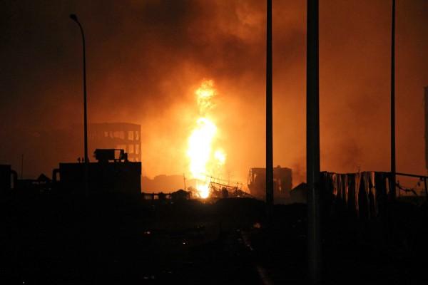 En hög eldsflamma nära en skadad byggnad vid explosionsplatsen i Tianjin 13 augusti 2015. Foto: STR/AFP/ Getty Images)