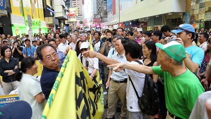 Lam Kwok-on pekas ut av åskådare efter hans försök att blockera Falun Gongs banderoller. (Foto: Pan Zaishu / Epoch Times)