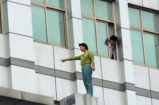 En man tittar ut från ett fönster på en kvinna som hotar att ta sitt liv genom att hoppa ner från en byggnad i staden Hefei i Kina. Många som lider av mentala sjukdomar får inte den hjälp de behöver i Kina. (Foto: AFP/Getty Images)

