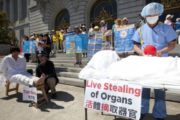 Skådespelare visar hur organstölder och tortyr utförs på Falun Gong-utövare, medan demonstranter håller upp skyltar vid en presskonferens i San Francisco City Hall den 5 september 2013, för att stödja en resolution i representanthuset mot organstölder i Kina. (Foto: Epoch Times)
