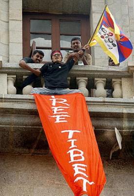 Indisk säkerhetspersonal försöker stoppa den tibetanske flyktingen Tenzin Tsundue som viftar med sin tibetanska flagga samtidigt som han vecklar ut en banderoll med texten ”Free Tibet.” Han ropar anti-kinesiska slogans uppifrån ett torn på det indiska vetenskapsinstitutet, där Kinas premiärminister Wen Jiabao deltar i ett möte, Bangalore 10 april 2005. (Foto: Dibyangshu Sarkar/AFP/Getty Images)