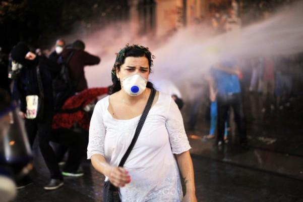 En demonstrant går undan vattenkanonerna på Istiklalgatan nära Taksimtorget i Istanbul, kvällen den 15 juni. Turkiets premiärminister Recep Tayyip Erdogan har uppmanat demonstranterna att lämna parken "i kväll", efter att ha lovat avbryta Taksimprojektet och bygget av artelleribarackerna. (Foto: Ozan Kose/ AFP)
