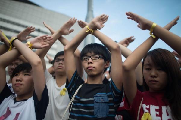 Den prodemokratiska studentgruppen Scholarism med dess samlande namn, Joshua Wong (mitten), gör en gest vid flagghissningsceremonin intill Gyllene Bauhinia-torget den 1 oktober 2014 i Hongkong. Tusentals demokratidemonstranter fortsätter att ockupera gatorna runtom i Hongkongs affärsdistrikt. Protestledarna hade satt den 1 oktober som deadline för uppfyllande av deras krav. De efterlyser öppna val och att Hongkongs högste ledare, Leung Chun-ying, ska avgå. (Foto: Anthony Kwan/Getty Images)
