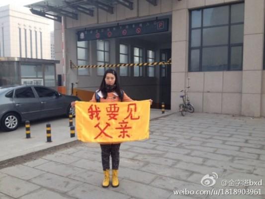 Högskolestudenten Bian Xiaohui håller upp en banderoll med texten, ”Jag vill träffa min far”, på gatan den 3 mars 2014. Bian, och hennes kusin som tog fotot, har fängslats. De åtalades den 12 december för att ha ”spridit propaganda om att Falun Gong förföljs” genom att ha lagt ut fotot på internet. (Foto: Skärmdump / Weibo.com) 