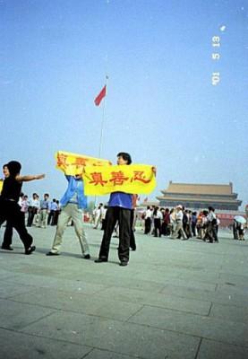 Falun Gong-utövare visar upp banderoller med texten "Sanning, godhet, tålamod" på Himmelska fridens torg medan en civilklädd polis rusar fram för att gripa dem. ()