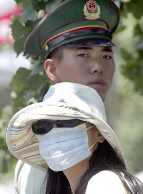 En kinesisk kvinna med munskydd stod bredvid en polisman vid en gata i Beijing den 11 juni 2004. Sars dödade cirka 800 människor i 32 länder i 2003. Den kinesiska regimen försökte att mörklägga sjukdomens utbrott i Guangdong, södra Kina. (Foto: AFP/Goh Chai Hin)