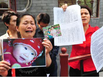 Zheng Shuzhen (t.v.) håller upp ett foto på sitt döda barnbarn Zhou Mengxin utanför hälsoministeriets klagomålsavdelning i Peking. Hon hävdar att barnets död, på grund av den förgiftade mjölken, aldrig har tagits itu med på ett acceptabelt sätt av lokalregeringen i Zhoukou i Henanprovinsen. (Foto: Frederic J. Brown/AFP/Getty Images)