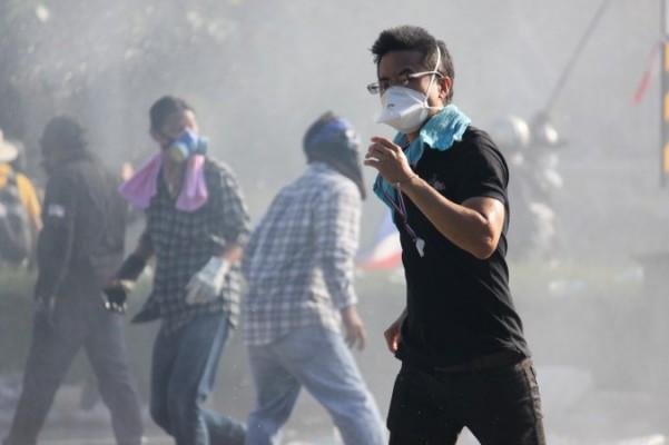 En demonstrant mot regeringen flyr tårgas och vattenkanoner under ett försök att bryta igenom en polisblockad nära Thailands regeringsbyggnad den 1 december 2013. (Foton: Cameron McKinley/Epoch Times)
