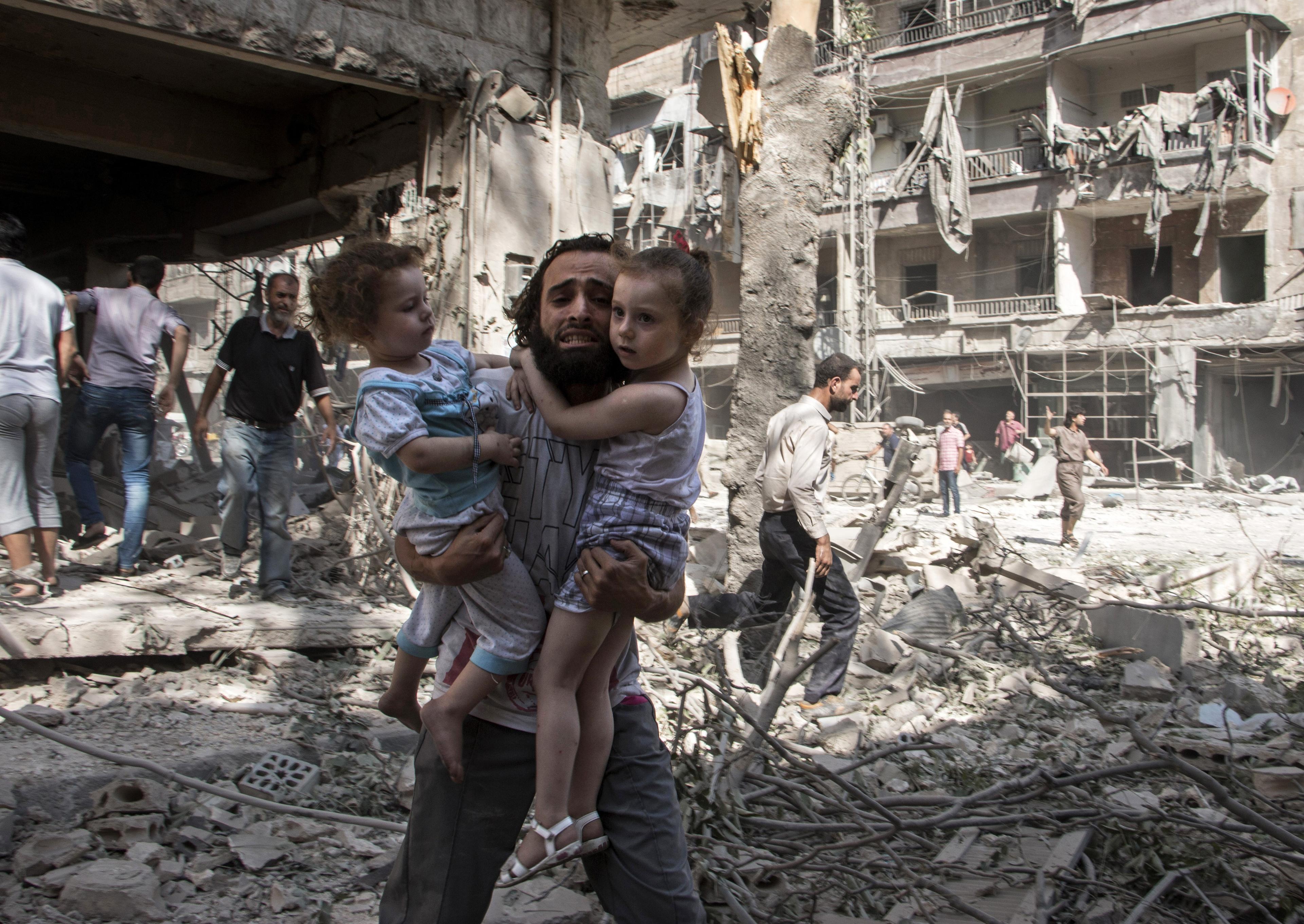 En man bär sina två döttrar över ruinerna efter en bombattack mot Aleppo i norra Syrien i september 2015. (Foto: Karam Al-Masri/AFP/Getty Image)