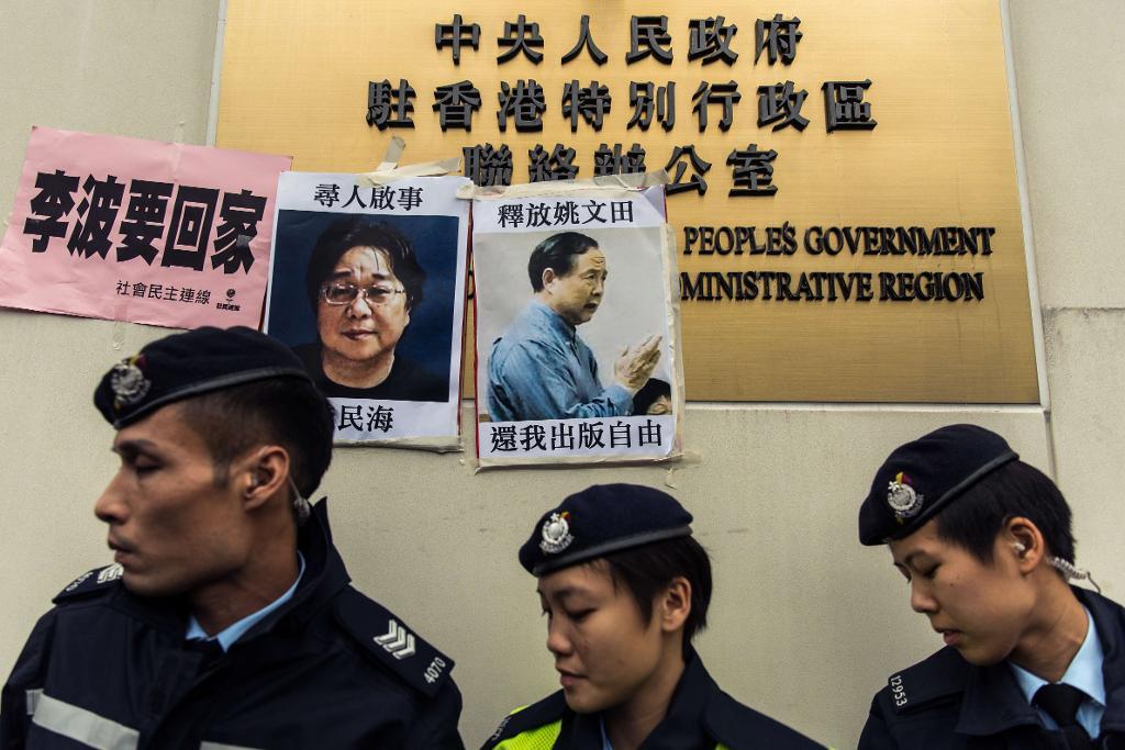Poliser passerar affischer med två försvunna personer, till vänster Gui Minhai och till höger Yau Wentian som jobbade på samma bokhandel och förlagshus i Hongkong. (Foto: Anthony Wallace/AP/TT)