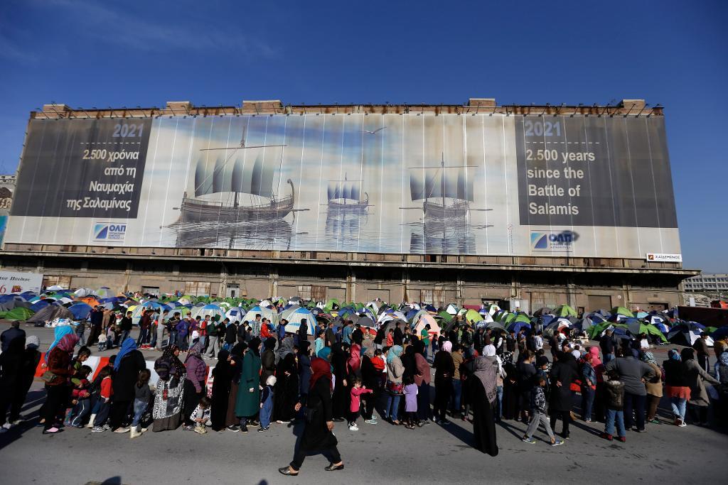 Flyktingar och migranter väntar på mathjälp i Piraeus. (Foto: Thanassis Stavrakis /AP/TT-arkivbild)
