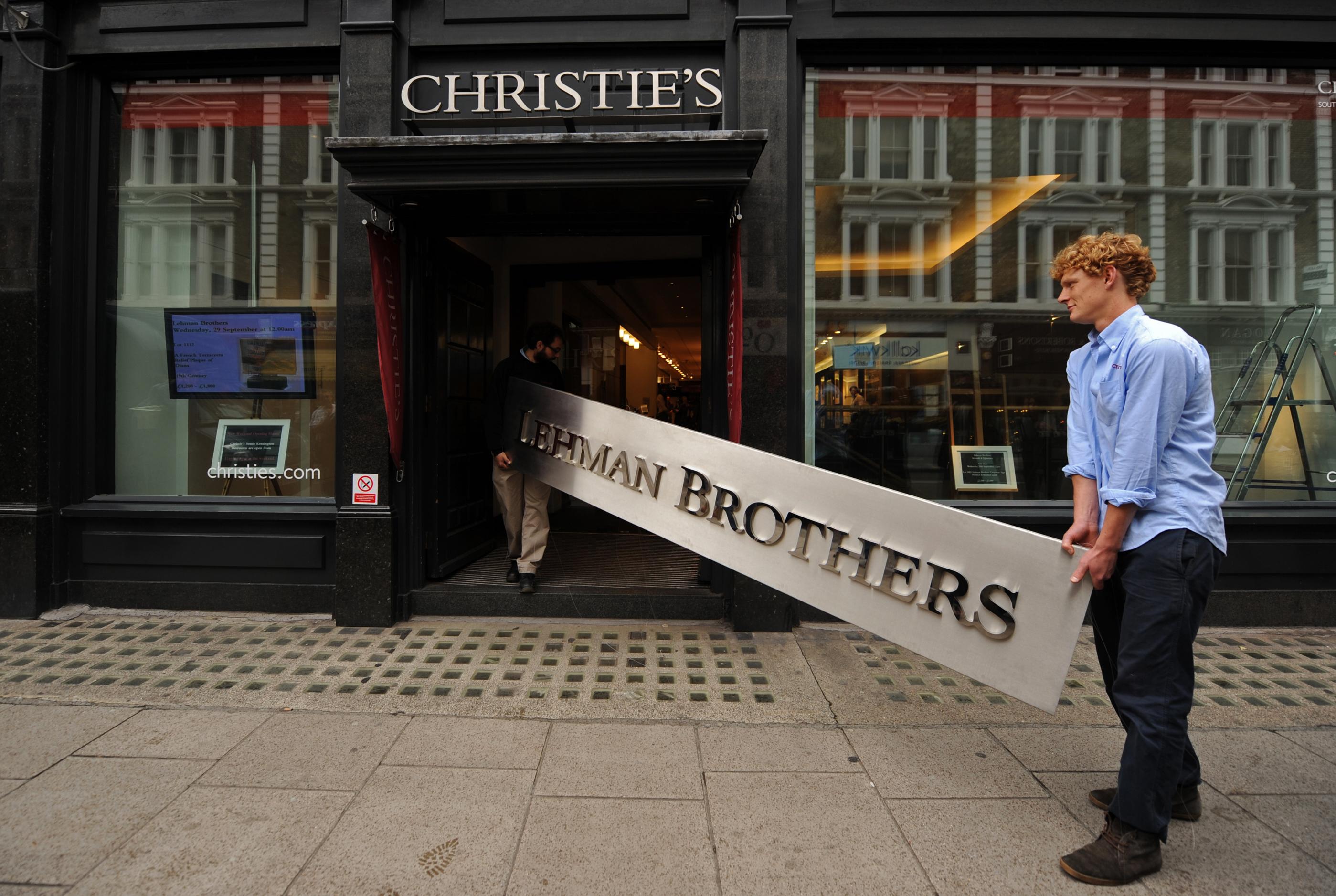 Anställda på auktionsfirman Christie's poserar med en nedtagen Lehman Brothers-skylt som såldes 2010. Det kommer dock inte att bli något sådant dramatiskt ögonblick för det skuldtyngda Kina, som när Lehman Brothers gick omkull, tror investeringsexperten Paul Krake, men läget är ändå dystert. (Foto: Ben Stansall/AFP/Getty Images)