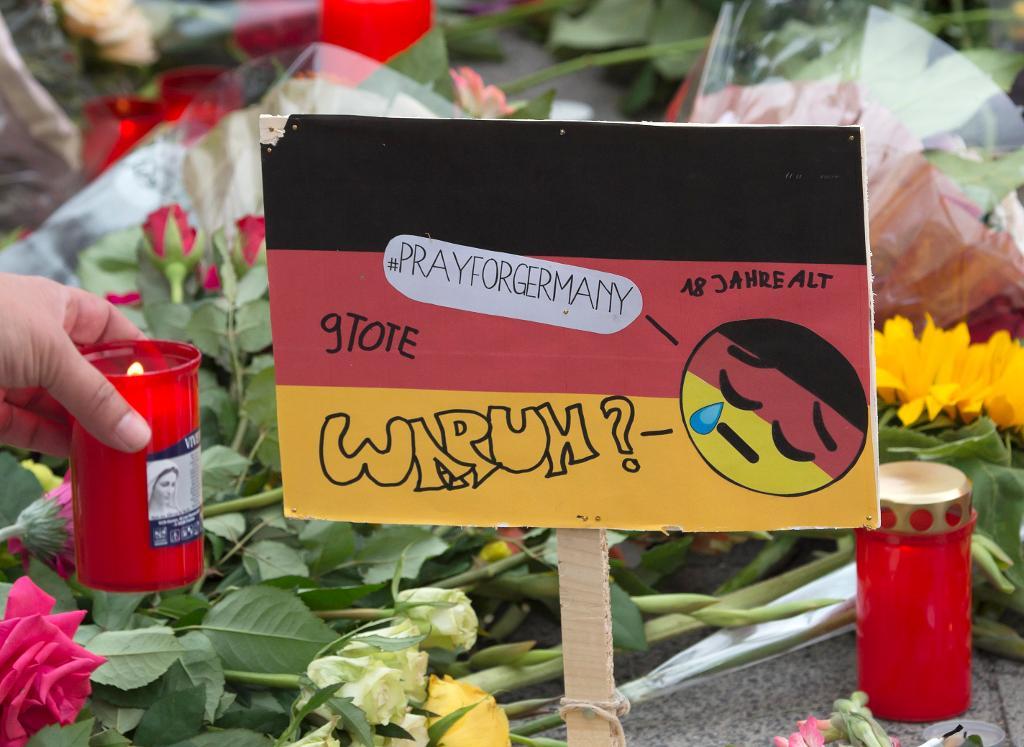 En kvinna tänder ett ljus vid en minnesplats utanför det köpcentrum i München där nio människor sköts ihjäl i fredags. (Foto: Jens Meyer/AP/TT)