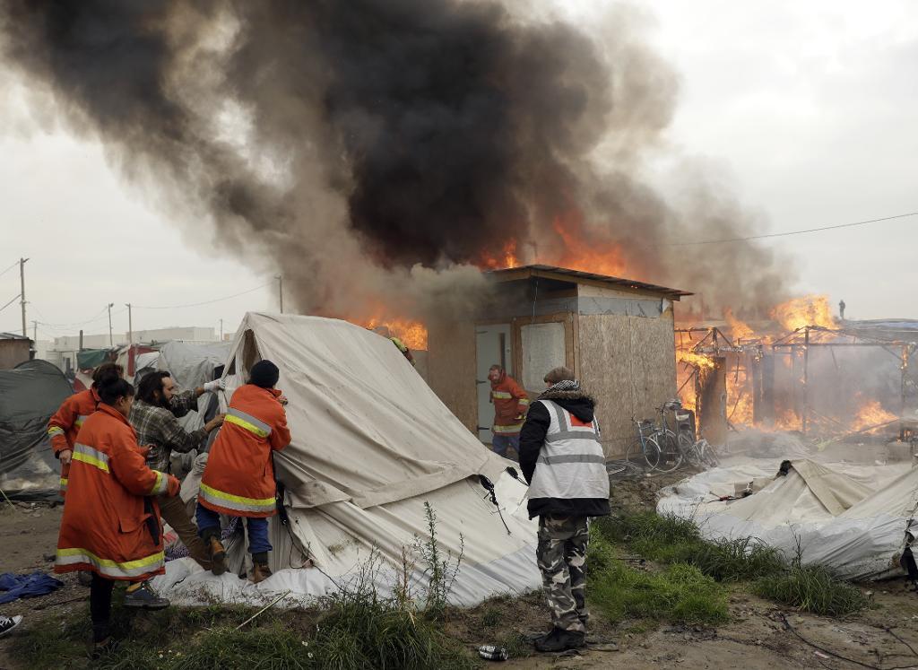 Volontärer försöker dra undan tält från brinnande skjul i "Djungeln". (Foto: Matt Dunham/AP/TT)