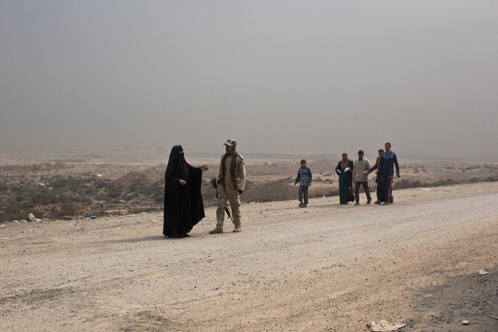 En kvinna pratar med en irakisk soldat vid en vägspärr söder om Mosul. IS-jihadister har de senaste dagarna tvingat människor från sina hem i samband med att gruppen tvingats dra sig tillbaka från byar nära den irakiska miljonstaden. Många av byborna har sedan dödats. (Foto: Marko Drobnjakovic/AP/TT)