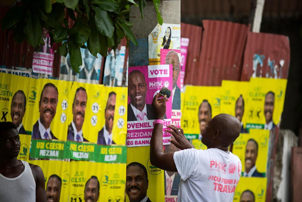 En Moise-anhängare sätter upp en kampanjaffisch inför valet. (Foto: Dieu Nalio Chery/AP/TT-arkivbild)