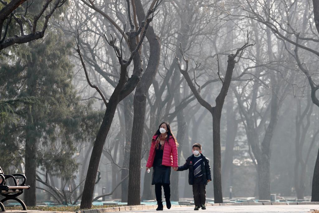 En kvinna och ett barn bär ansiktsmasker till skydd för smoggen i Peking. (Foto: Andy Wong/AP/TT)