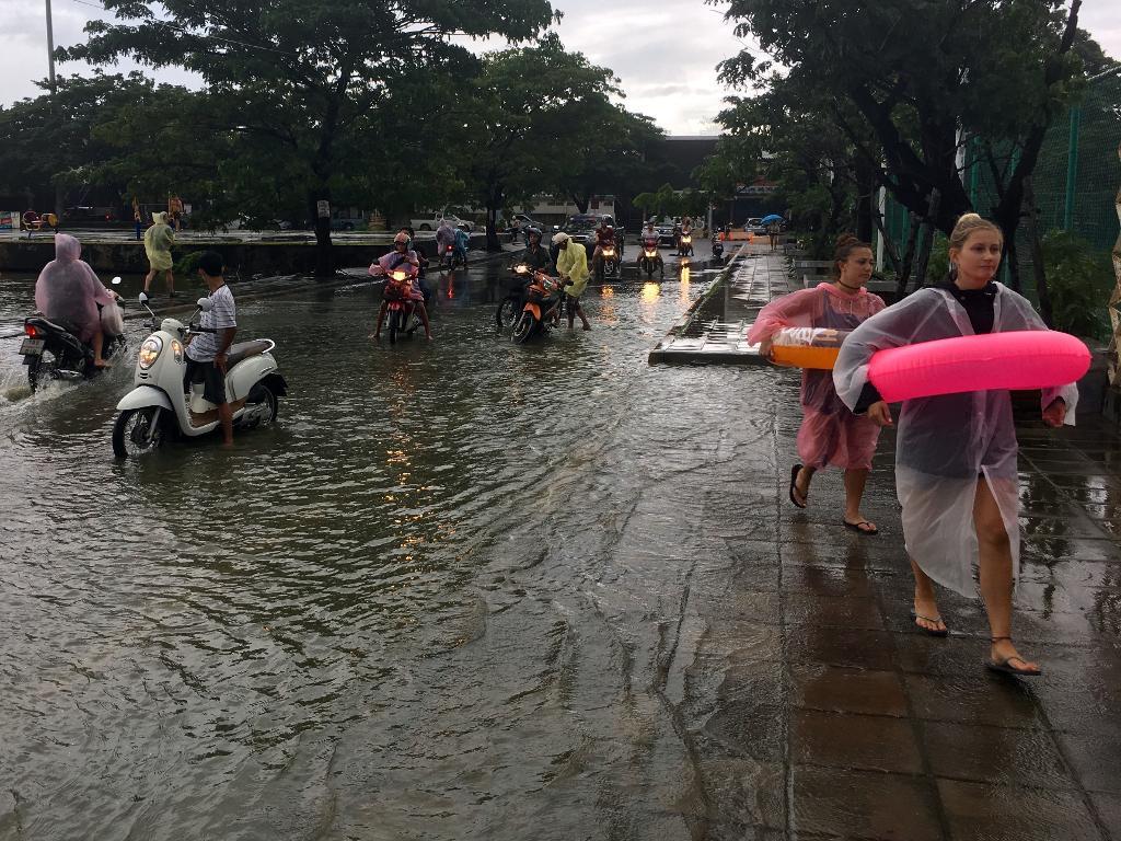 Turister med flytringar går längs en översvämmad gata på Koh Samui i Thailand. (Foto: Adam Schreck/AP)