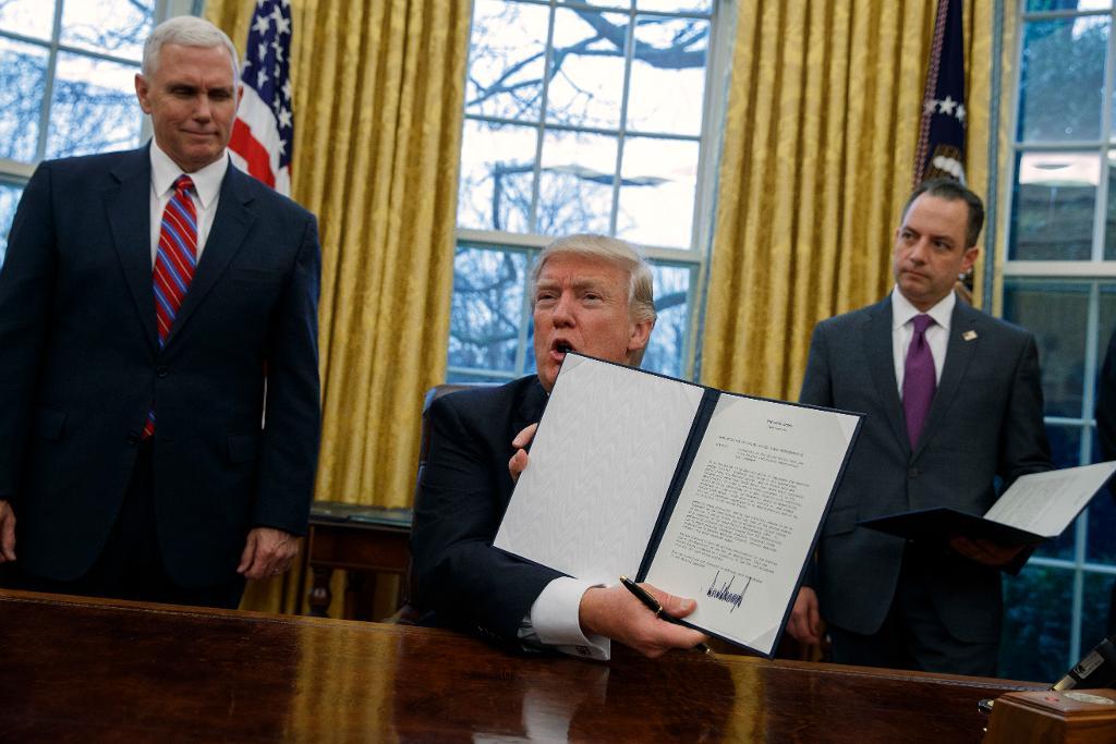 Donald Trump med den exekutiva ordern om att USA ska lämna frihandelsavtalet TPP. Till vänster vicepresident Mike Pence och till höger stabschefen Reince Priebus. (Foto: Evan Vucci/AP/TT)