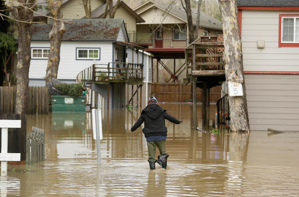 Häftiga oväder har orsakat översvämningar på flera håll i Kalifornien. I Guerneville vadar en invånare genom vattnet på stadens gator. (Foto: Eric Risberg /AP/TT)