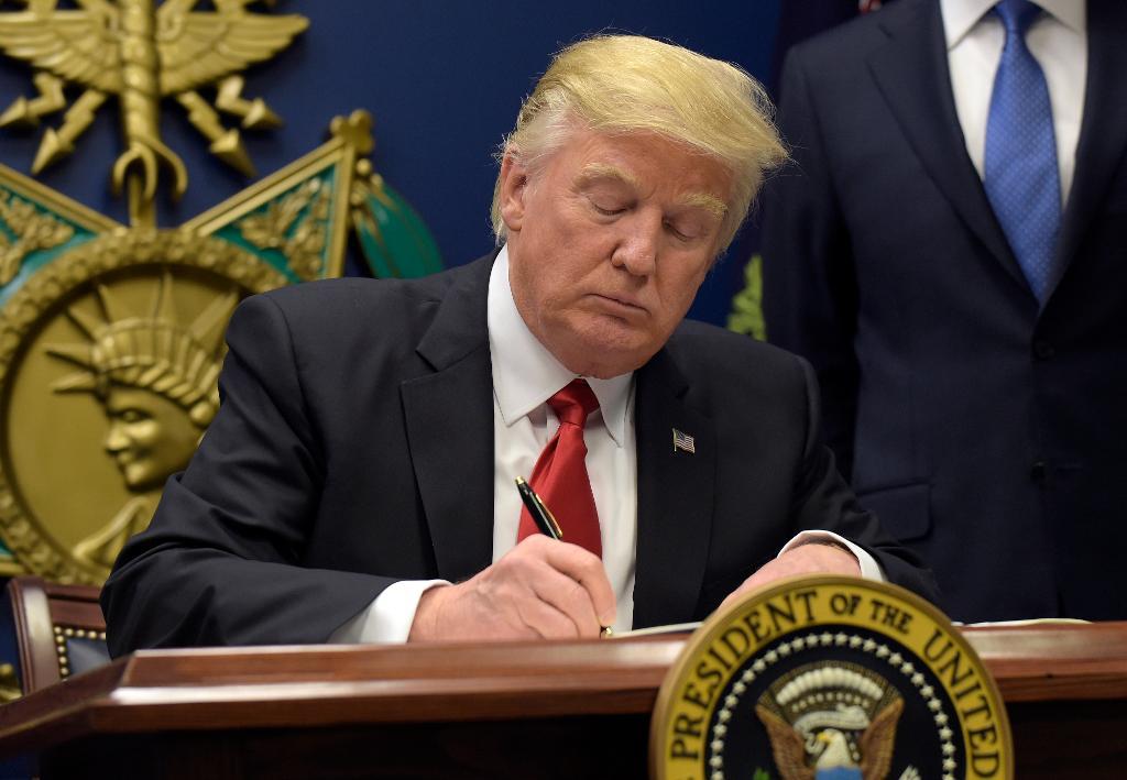 President Donald Trump skriver på en presidentorder om att förstärka granskningen av migranter och flyktingar som i framtiden kommer till USA. (Foto: Susan Walsh/AP/TT)