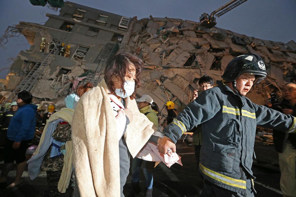 En kvinna leds bort från det kollapsade bostadshuset i Tainan efter jordbävningen. (Foto: AP)