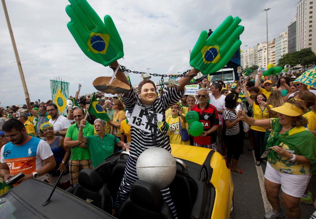 En demonstrant har klätt ut sig till president Dilma Rousseff i fångkläder på Copacabana i Rio de Janeiro. (Foto: Silvia Izquierdo /AP/TT)