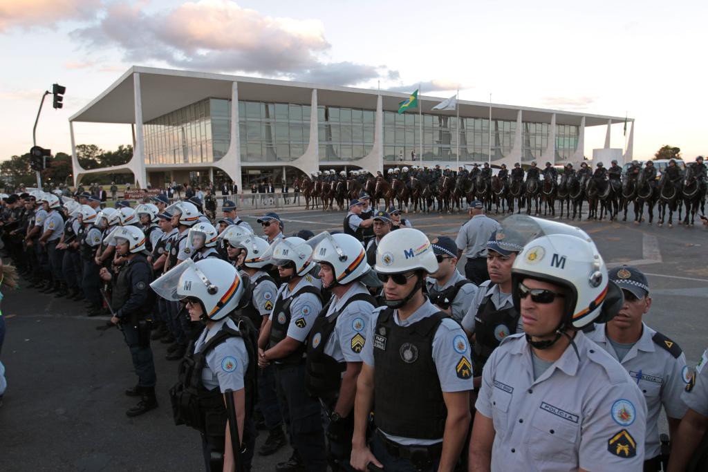 Polis vaktar utanför presidentpalatset medan demonstrranter kräver president Dilma Rousseffs avgång. (Foto: Joedson Alves/AP/TT)
