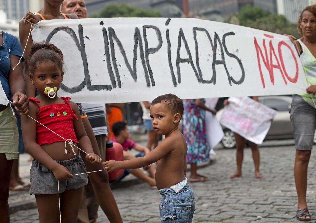 På banderollen bakom barnen står det "OS nej" på portugisiska. Kostnaderna för de olympiska spelen i Rio de Janeiro har lett till protester runtom i Brasilien. (Foto:Silvia Izquierdo/AP/TT)