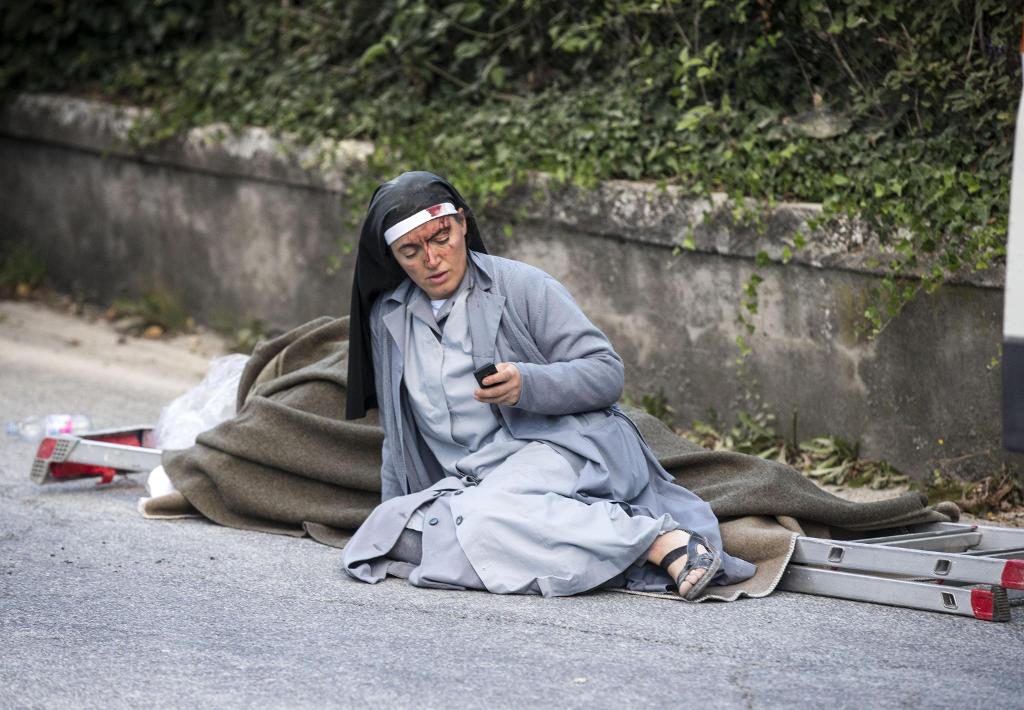 Syster Mariana, nunna från Albanien, kollar sin mobiltelefon medan hon sitter vid ett av jordbävningsoffer. (Foto: Massimo Percossi /AP/TT)