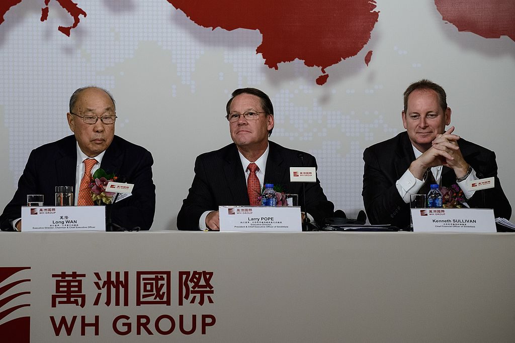 På en presskonferens i Hongkong 2014 ses Wan Long, ordförande för WH Group, med två av Smithfield Foods högsta chefer Larry Pope och Kenneth Sullivan. (Foto: Philippe Lopez/AFP/Getty Images)