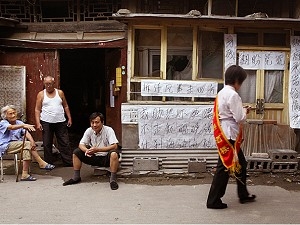 Kineser sitter intill en igenbommad butik med protestbanderoller, som finkänsligt kritiserar demoleringen av det anrika Peking-grannskapet. Förberedelserna inför OS 2008 har lett till att bostadsägare och hyresgäster vräkts, vilket kränker kinesisk lag och internationella normer i rätten att hysa en bostad. Detta har inneburit vräkta bostadsägare och hyresgäster, som inte har någon laglig utväg och ofta inte får någon kompensation. (Frederic J. Brown/AFP/Getty Images)