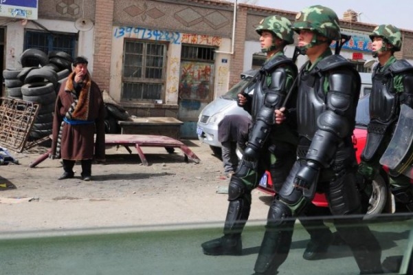 Skyltar på kinesiska syns på denna bild av en tibetansk man i traditionella kläder som betraktar kinesiska paramilitärer i kravallutrustning i Guomaying på den tibetanska platån. Kinas politik tycks inriktad på att ersätta de etniska minoritetsspråken med mandarin. (Foto: Frederic J. Brown/AFP/Getty Images)