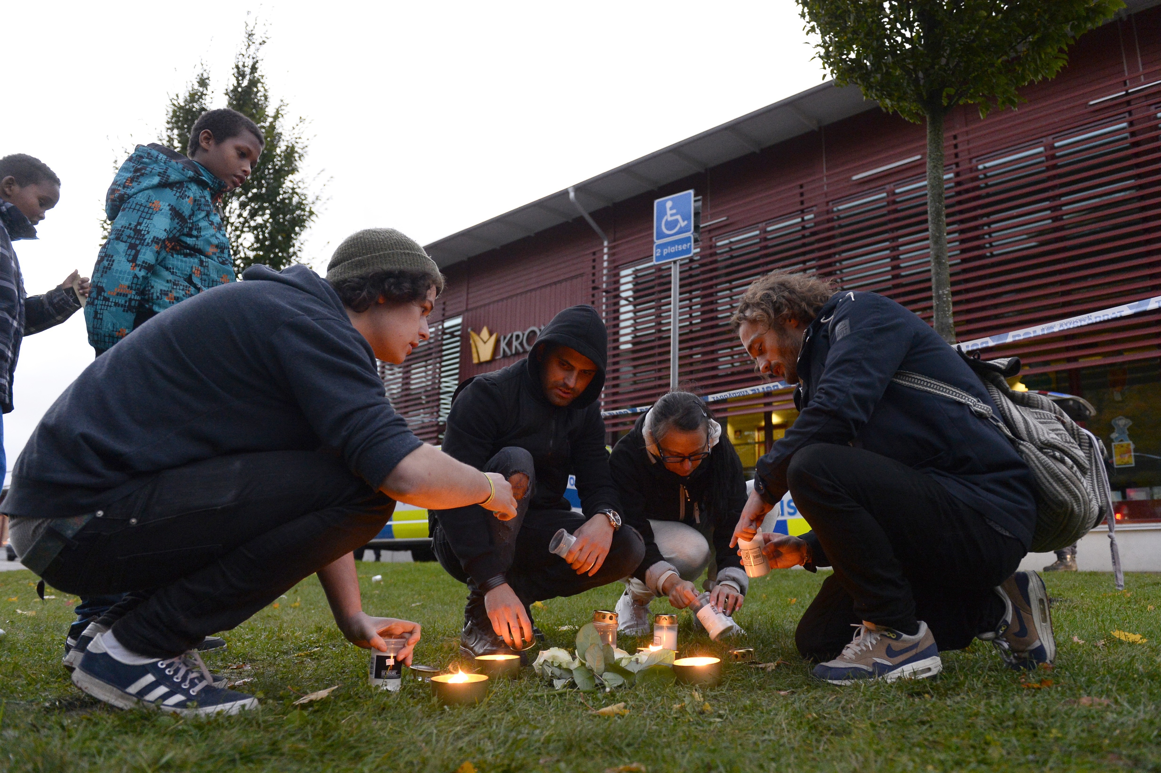 Barn tittar på när några personer tänder ljus utanför skolan där knivdåden utfördes, 22 oktober 2015. En maskerad man dödade två och skadade två allvarligt innan ha sköts av polis. Dåden uppges ha haft rasistiska motiv.
(Foto:  Jonathan Nackstrand       /AFP/Getty Images)