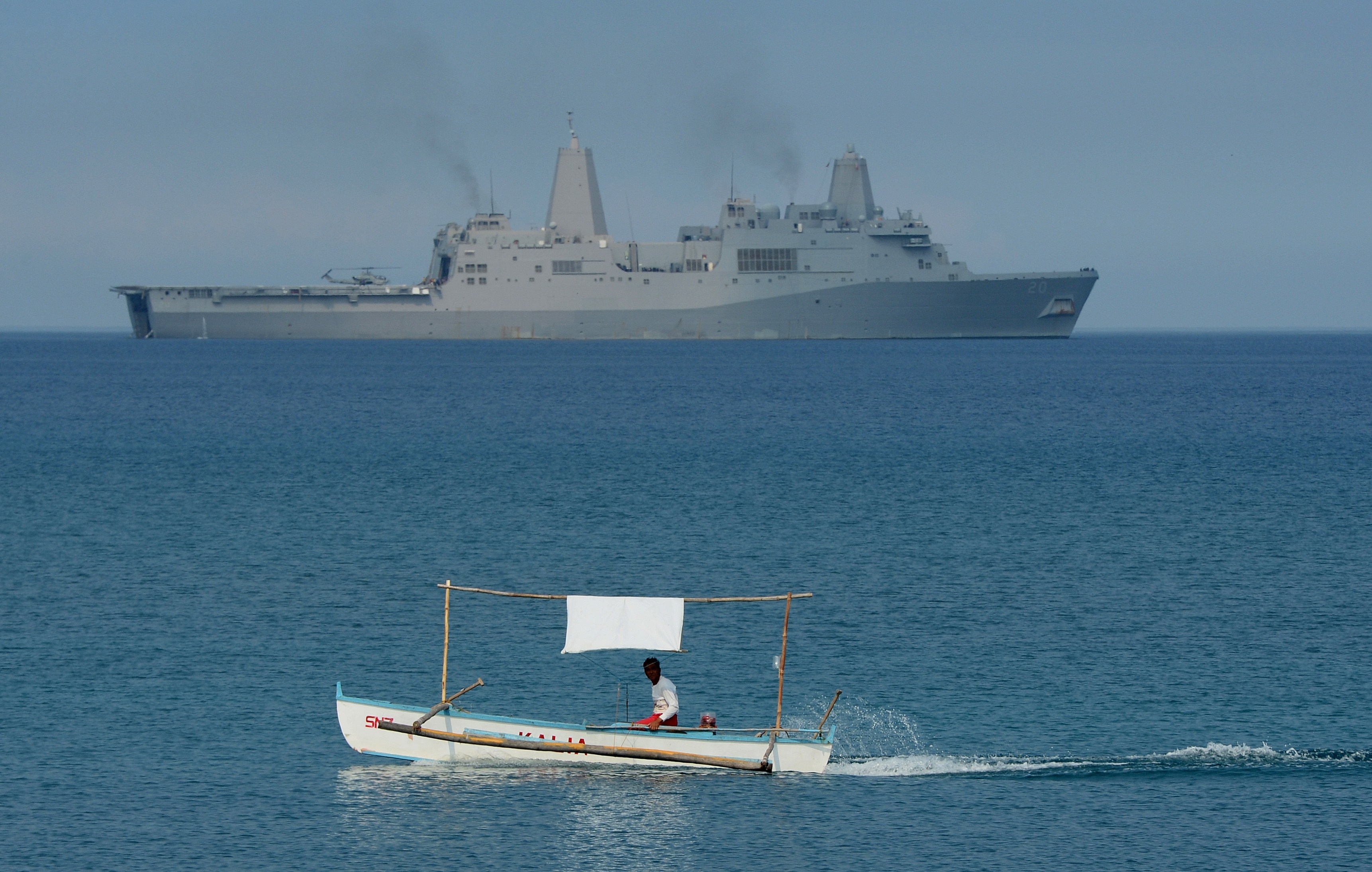 En filippinsk fiskare framför ett amerikansk militärfartyg, under gemensamma övningar mellan USA och Filippinerna i april 2015. (Foto: Ted Aljibe/AFP/Getty Images)