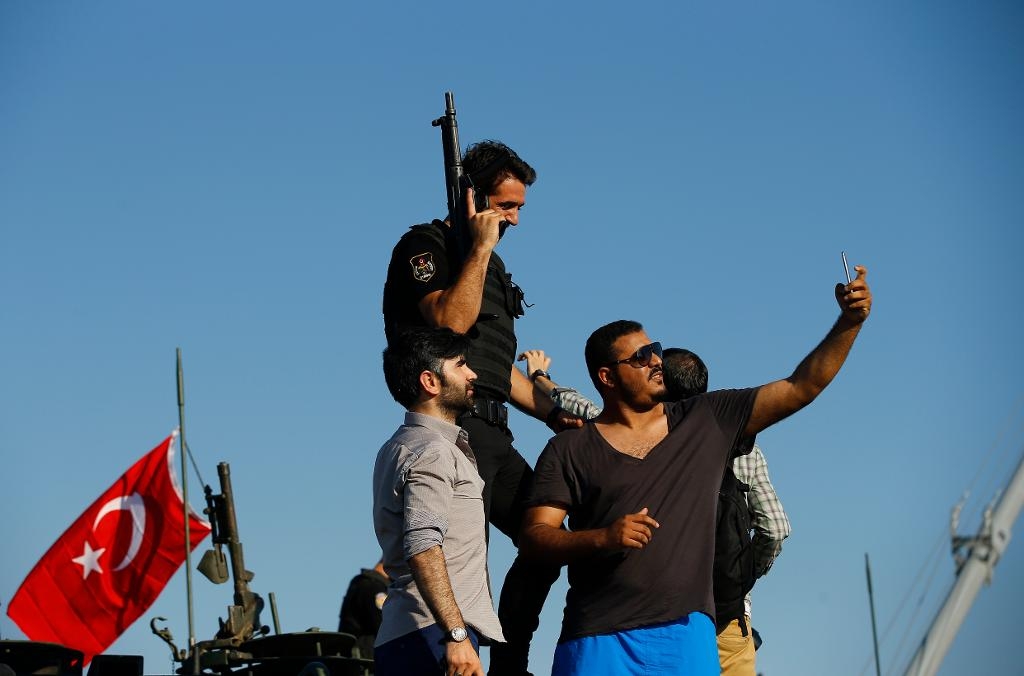 En polisman omgiven av civila, alla trogna presidenten Erdogan, står på en stridsvagn som övergivits av militärer i Istanbul. (Foto: Emrah Gurel/AP/TT)