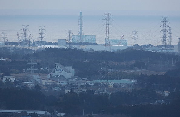 I bakgrunden syns Fukushima Daiichi kärnkraftverk, den 11 mars 2016 - fem år efter en av världshistoriens allvarligaste kärnkraftsolyckor som tillsammans med tsunamin kostade runt 18 500 liv. Nu funderar Japan på att återgå till kärnkraft.  (Foto: Jiji Press/AFP/Getty Images)