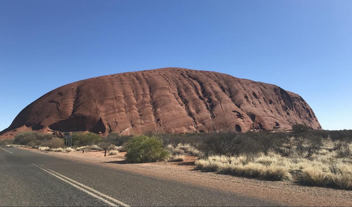 För den som närmar sig med bil tornar klippan upp sig på långt håll. Spåren på berget har enligt aboriginernas berättelser bildats när ödle- och ormvarelser krigade.  Foto: Henrik Samuelsson/TT