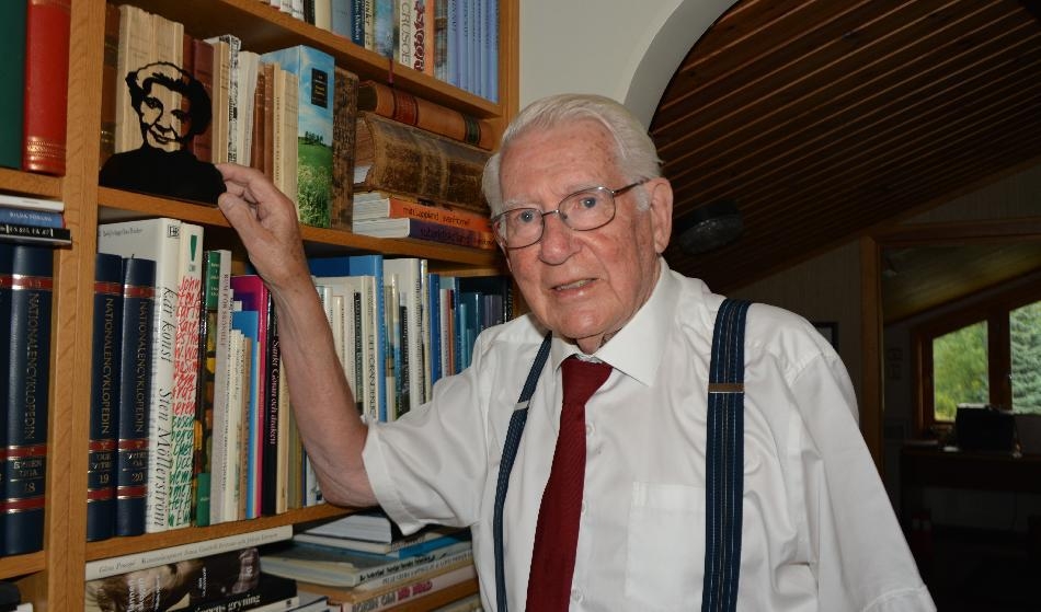 Thage G Peterson framför hyllan med böcker av och om Elin Wägner i hans hus i Nacka i Stockholm. Den grafiska grafiska bilden framför böckerna föreställer Elin Wägner. Foto: Lars Liljesvärd