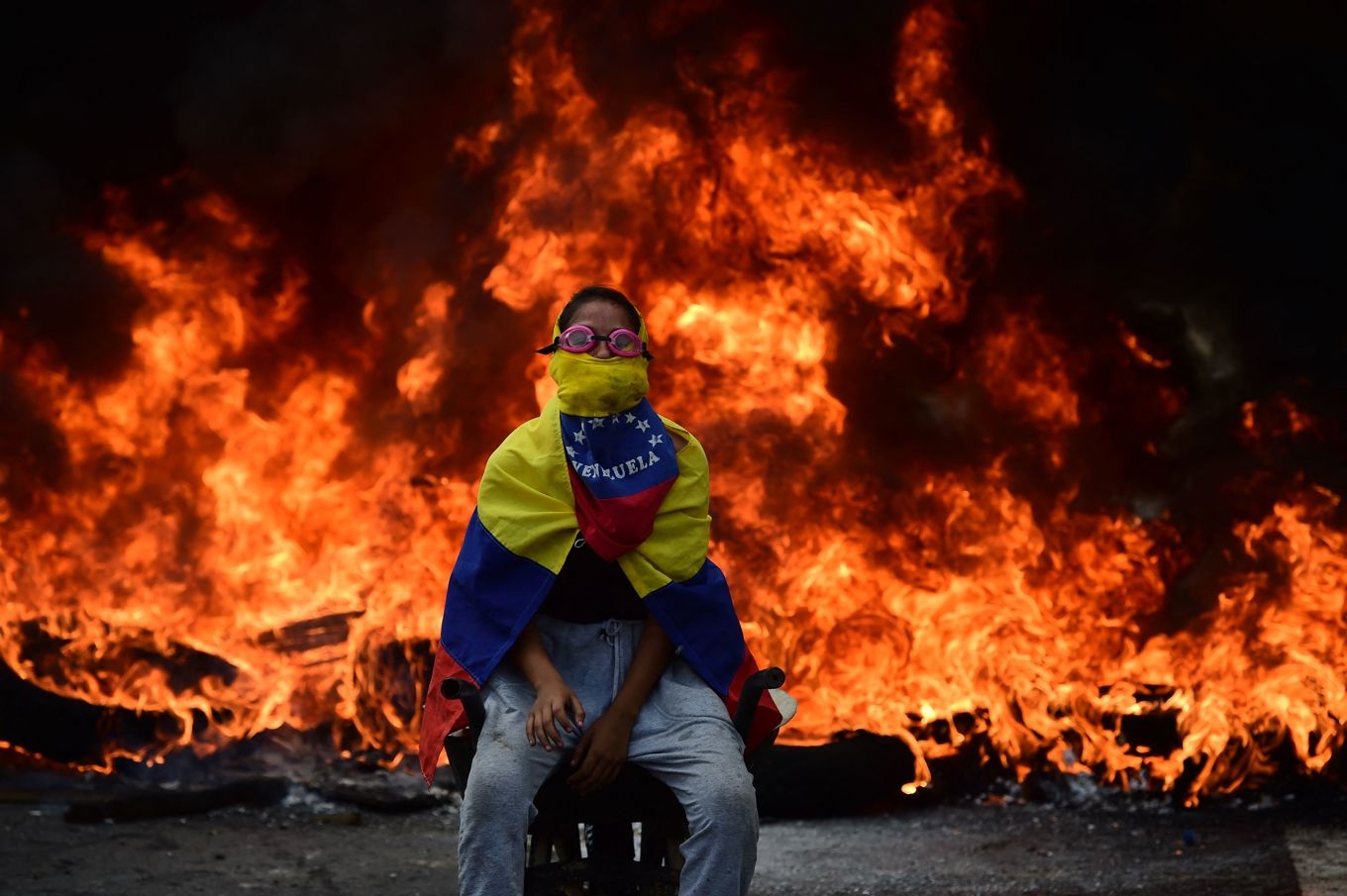 En oppositionsaktivist syns framför en brinnande barrikad i Venezuelas huvudstad Caracas, under de enorma protesterna 2017 mot den socialistiska regimen som ruinerat landet. Foto: Ronaldo Schemidt/AFP via Getty Images