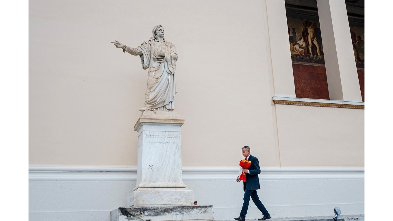 En man ses här passera förbi den staty föreställande den grekiske nationalhjälten Rigas Feraios som är placerad utanför universitetet i Aten. Foto: Angeloz Tzortzinis/AFP via Getty Images