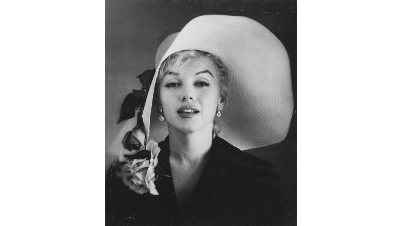 Ett svartvitt fotografi av Marilyn Monroe, iförd en stor vit stråhatt med rosor, taget av Carl Perutz 1958. Fotot har ett uppskattat pris på 700–900 dollar. Enligt samstämmiga uppgifter var det DiMaggio som såg till att Marilyns grav alltid pryddes av färska röda rosor – ett löfte som han höll i över 20 år, fram till sin egen död, genom att låta en florist leverera dem tre gånger i veckan. Foto: Christie’s Images LTD. 2025